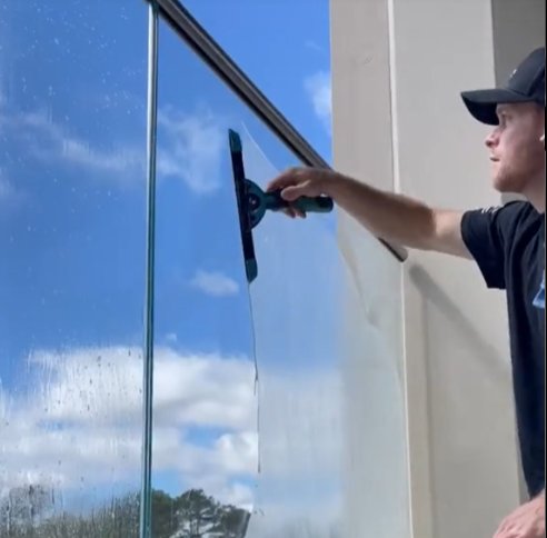 Perfect Pane technician squeegeeing a glass balcony railing clean in the North Bay