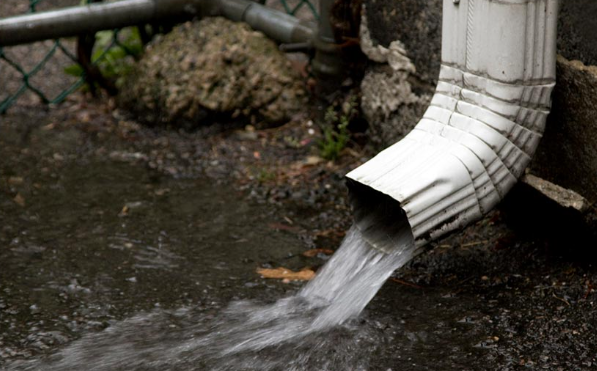 Water flowing freely out of a clean downspout after gutter cleaning