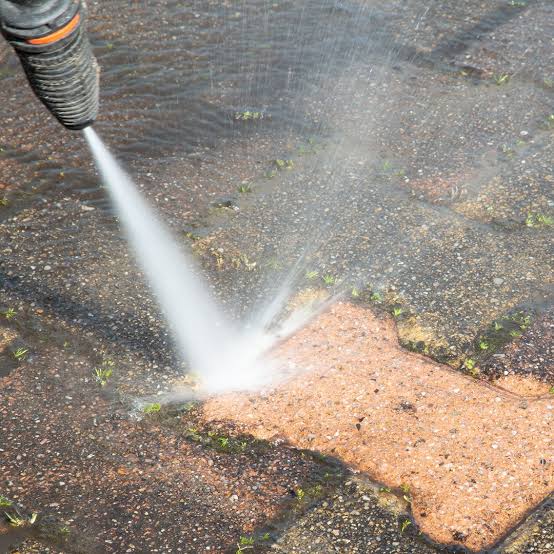 Pressure washer nozzle blasting grime and moss off a paver surface