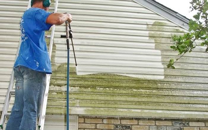 Vinyl siding being power-washed clean of algae stains